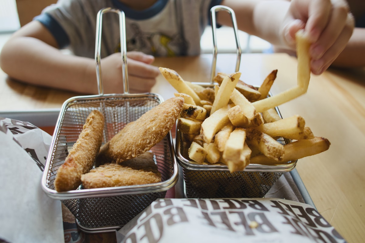 Hände greifen nach Pommes und Chicken Tenders